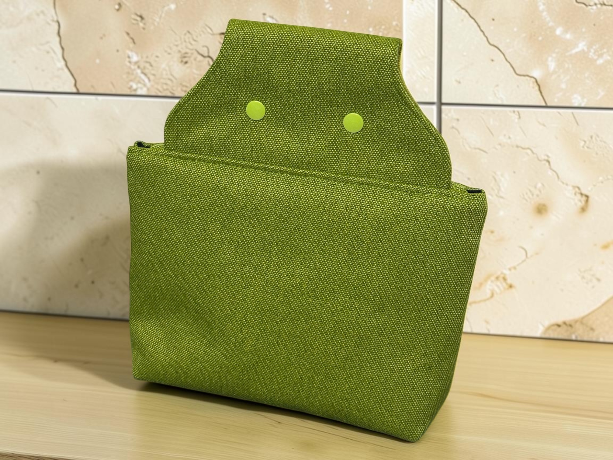Green fabric storage box on a light wooden surface, with a curved lid and two circular fasteners visible on the side.