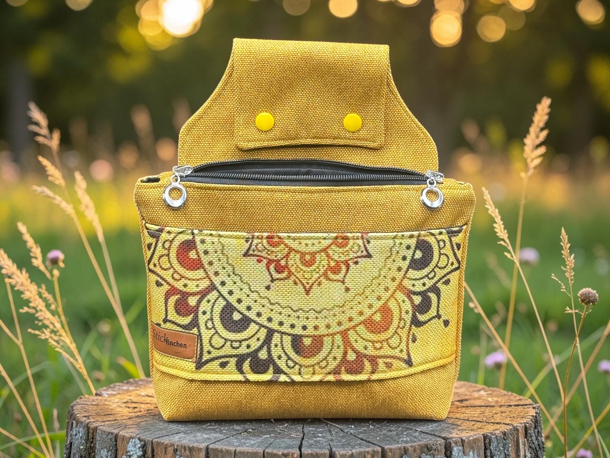 Yellow patterned backpack resting on a tree stump in a sunlit field outside.