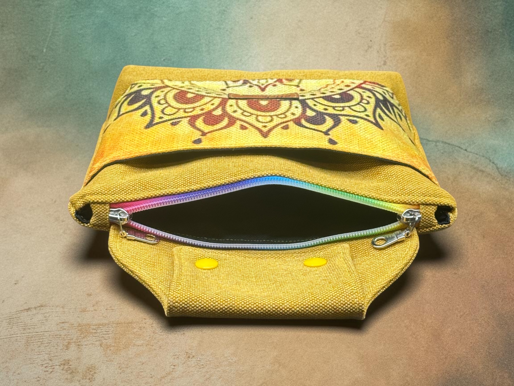 Yellow backpack with a decorative patterned flap and rainbow zippers, viewed from the top.