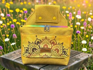 Yellow backpack with a decorative mandala pattern sits on a weathered wooden bench in a field of yellow and white flowers.