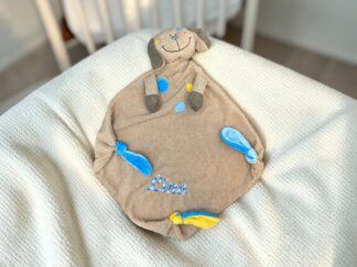 Beige plush dog with gray ears and blue/yellow polka dots sits on a cream textured blanket; 'Lina' embroidered in blue.